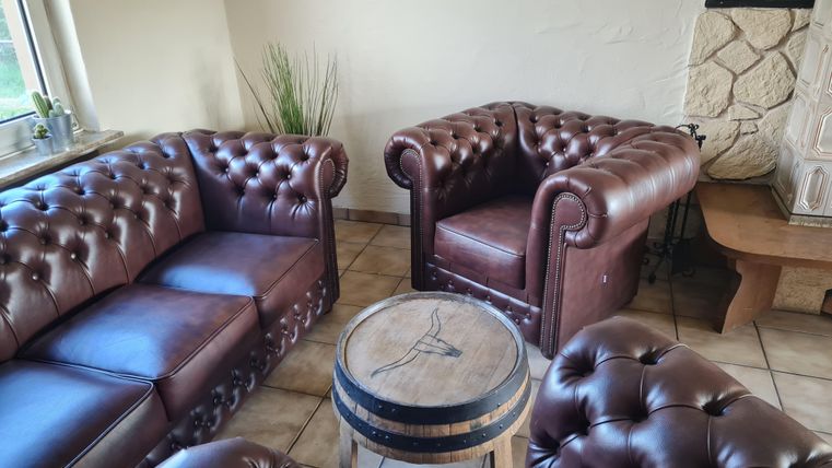 Een uitnodigende woonkamer met bruine, gestoffeerde Chesterfield-meubels en een kleine tafel in het midden. De sfeer is gezellig en stijlvol.