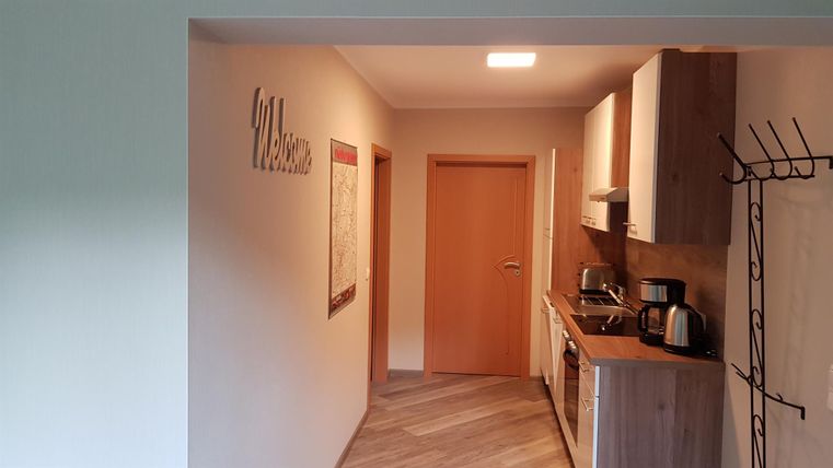 Een moderne keuken met houten kasten en lichte muren. Op de achtergrond ziet men een gezellige ingang.