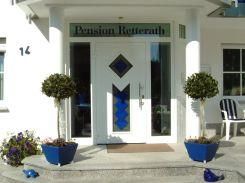 Une entrée accueillante pour la pension Rotterath avec une porte moderne et des plantes décoratives. Les couleurs bleu et blanc dominent le design.