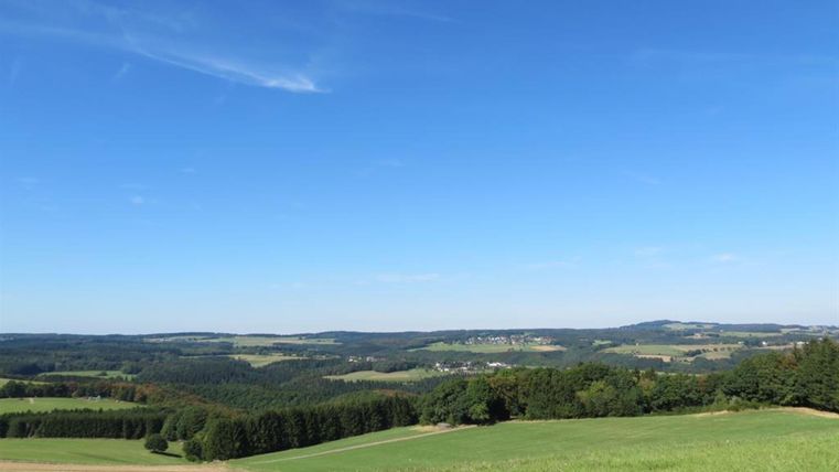 Eine weite Landschaft mit sanften Hügeln und üppigem Grün. Der Himmel ist klar und blau, was eine friedliche Atmosphäre schafft.