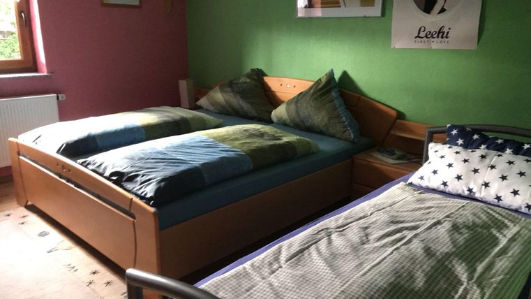 A simple bedroom with two beds and colorful bed linens. The walls are painted green and pink, and there is a window that floods the room with daylight.