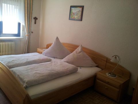 A cozy bedroom with a double bed and two pillows. Next to the bed is a nightstand with a lamp.