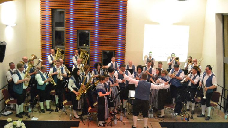 Een blaasorkest geeft een concert. De muzikanten dragen traditionele kleding en bespelen verschillende instrumenten.