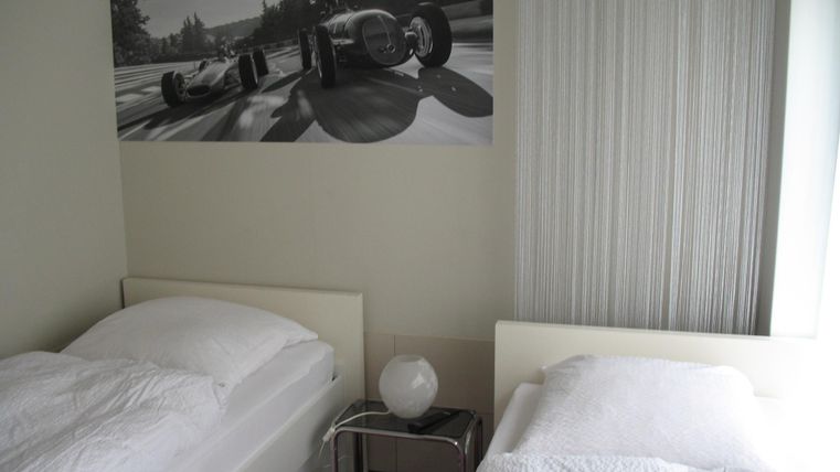 Ein modernes Schlafzimmer mit zwei Einzelbetten und einem Nachttisch. An der Wand hängt ein großes Bild von einem Rennwagen auf einer Rennstrecke.
