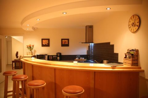 Une cuisine moderne avec un bar en bois et un éclairage lumineux. L'aménagement de la cuisine est minimaliste et accueillant.