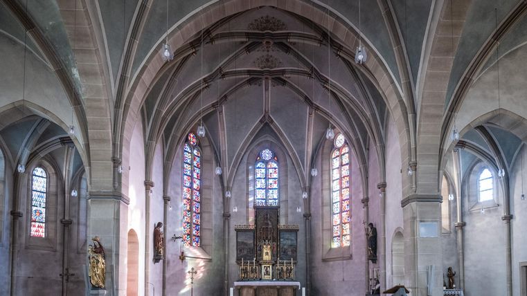 Eine beeindruckende Kirche mit hohen Gewölben und farbigen Fenstern. Der Altarbereich ist zentral und begehrt Aufmerksamkeit.