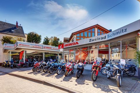 Ein Motorradgeschäft mit verschiedenen Motorrädern vor einem modernen Gebäude. Das Geschäft ist als Honda und Yamaha gekennzeichnet.