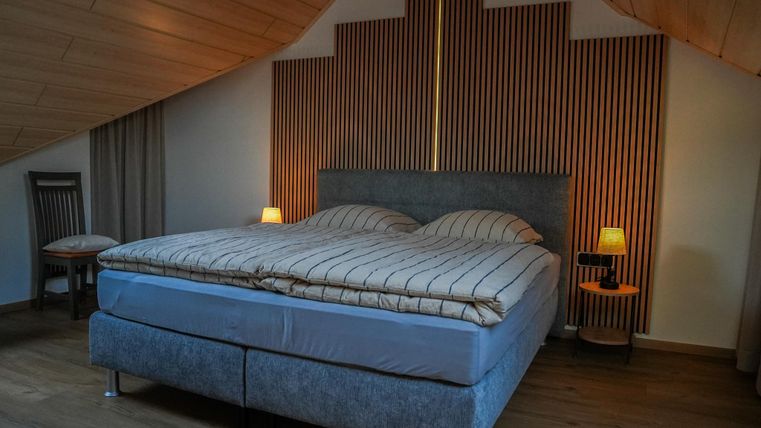 Een gezellige slaapkamer met een groot bed en houten wandbekleding. Zachte verlichting creëert een uitnodigende sfeer.