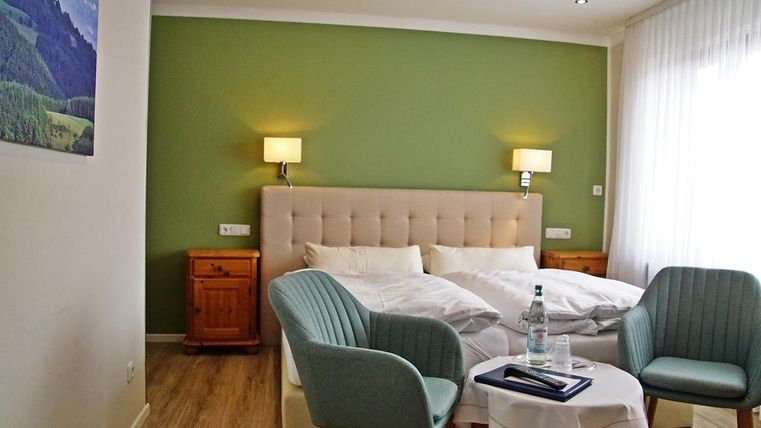 Une chambre confortable avec un grand lit et des murs verts doux. Deux fauteuils confortables et une petite table sont également présents.