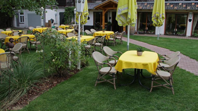 Ein einladender Außenbereich mit gelben Tischen und Stühlen auf einer grünen Wiese. Sonnenschirme sorgen für Schatten und eine gemütliche Atmosphäre.