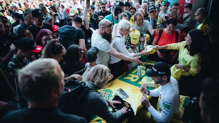 Eine große Menschenmenge bei einer Autogrammstunde. Fans interagieren mit einem Fahrer, während sie Autogramme und Merchandise erhalten.