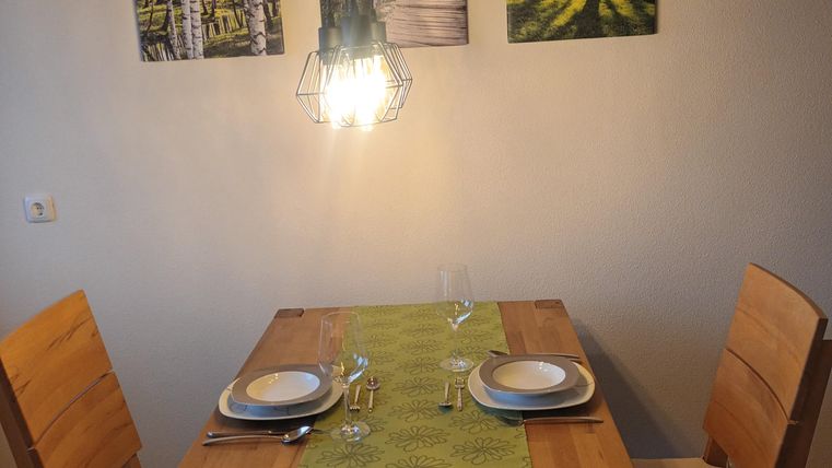 Een gezellige eetruimte met een houten tafel en twee stoelen. Aan de muur hangen foto's van boslandschappen en een stijlvolle lamp zorgt voor warm licht.