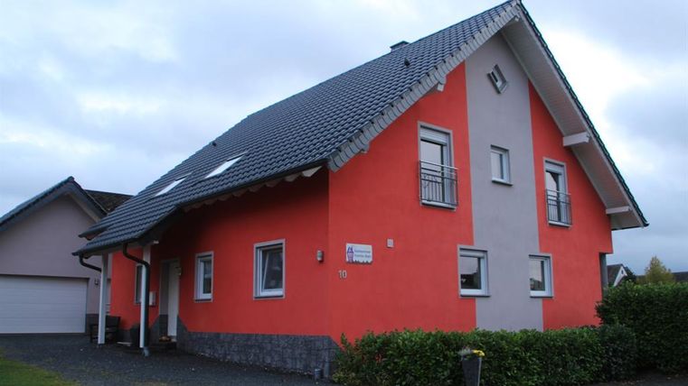 A modern house with a red and gray facade. It has a slanted roof and windows that let light in.