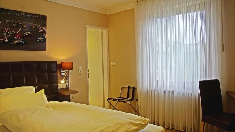 Une chambre d'hôtel lumineuse avec un lit simple et une table. La chambre dispose de grandes fenêtres avec des rideaux et d'une ambiance moderne.