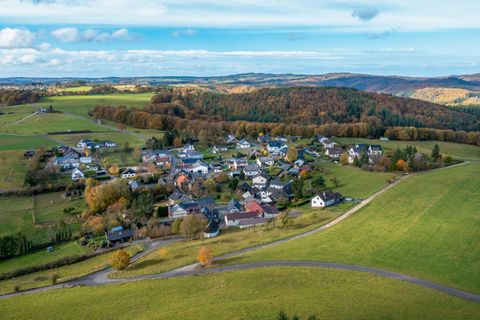 Eine malerische Landschaft mit einem kleinen Dorf, umgeben von grünen Feldern und Wäldern. Der Himmel ist klar und blau.