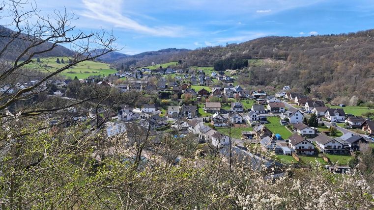 Eine malerische Landschaft mit einer kleinen Stadt, umgeben von grünen Wiesen und Hügeln. Der klare Himmel und die ruhige Atmosphäre schaffen ein harmonisches Gesamtbild.