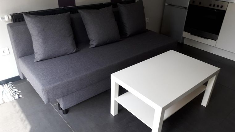 Ein modernes Wohnzimmer mit einem grauen Sofa und mehreren Kissen. Ein weißer Couchtisch steht davor.