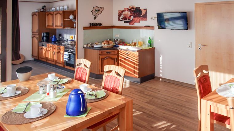 Eine gemütliche Küche mit einem Esstisch und Stühlen. Auf dem Tisch sind Geschirr und eine Kaffeekanne zu sehen.