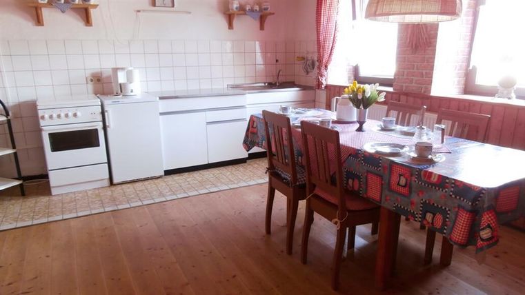A cozy kitchen with a dining table and chairs. On the table are dishes and a flower vase, while the room is bright and inviting.