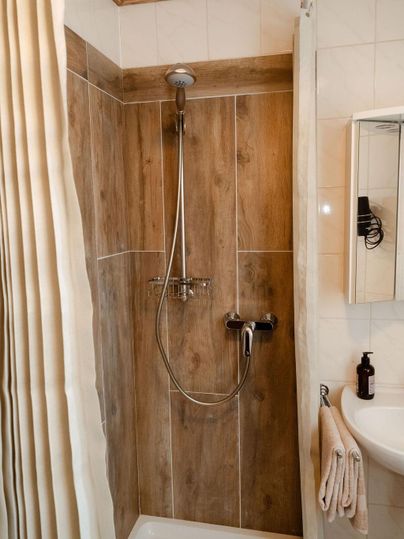 Eine moderne Dusche mit Holzoptik und weißen Fliesen. Es gibt eine Duschbrause, einen Handtuchhalter und ein Spiegel.