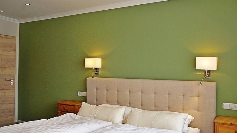 Une chambre moderne avec une teinte de peinture murale vert clair. Le lit a une tête de lit rembourrée et il y a des lampes de chevet sur les murs.