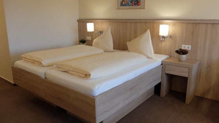 Een gezellige tweepersoonskamer met twee bedden en lichte beddengoed. De muren zijn in neutrale kleuren gehouden, en er is een kleine nachttafel lamp en een kunstwerk aan de muur.