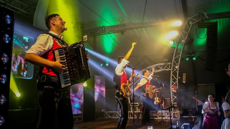 A band is playing on a stage with colorful lights. Musicians with an accordion and a guitar create a good atmosphere.