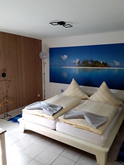 Een moderne slaapkamer met een tweepersoonsbed en twee grote kussens. Aan de muur hangt een afbeelding van een idyllisch eiland met helder water en palmbomen.