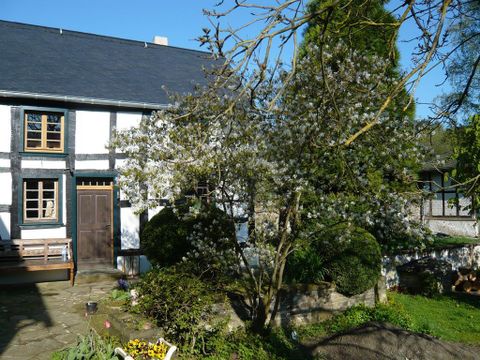 A traditional timber-framed house surrounded by blooming trees and a well-manicured garden. The sky is clear and the atmosphere is inviting.