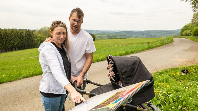 Ein Paar mit Kinderwagen betrachtet eine Karte in einer ländlichen Umgebung.