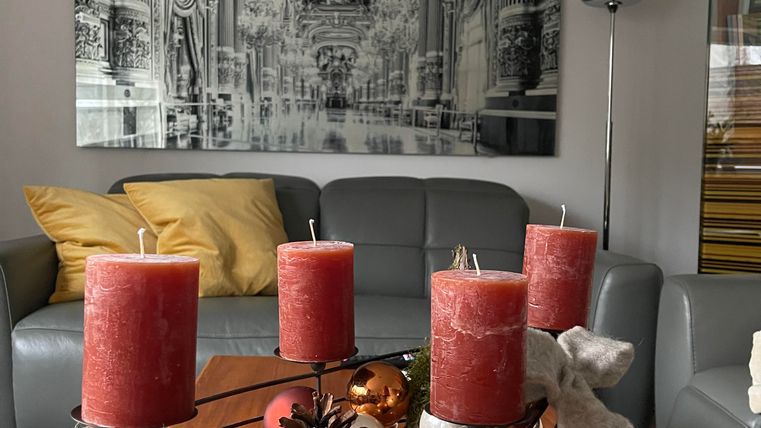 Un salon confortable avec un canapé gris et des coussins colorés. Sur la table se trouve un panier décoratif avec des bougies rouges et des matériaux naturels.