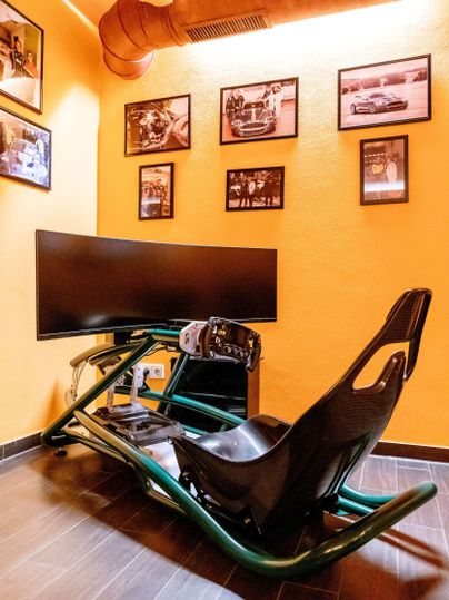 Een gameroom met een racestoel en een groot beeldscherm. Aan de muren hangen foto's van auto's.