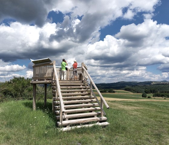 Zwei Personen stehen auf einer Holzplattform und blicken in die weite Landschaft. Der Himmel ist teils bewölkt, teils blau., © Siegfried Müller