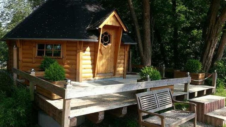 Eine gemütliche Holzhütte mit einem runden Dach und einer einladenden Terrasse. Umgeben von Bäumen und Pflanzen, bietet sie eine ruhige Atmosphäre.