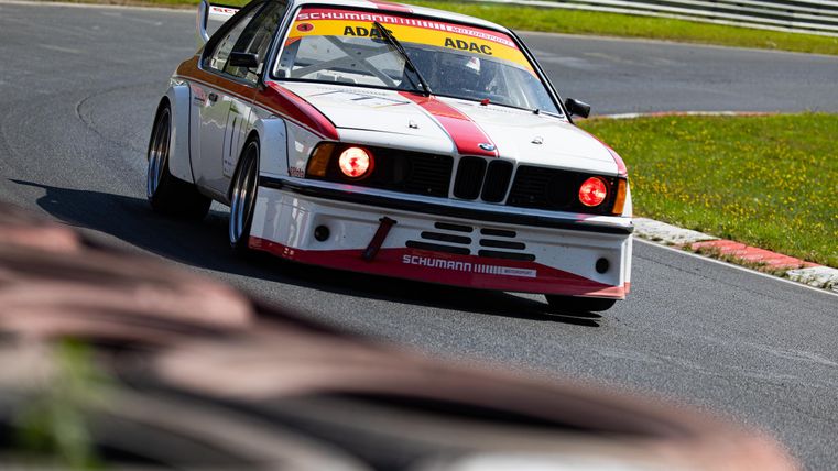 Ein Rennwagen fährt auf einer Strecke, umgeben von grünen Wiesen. Die Karosserie hat ein auffälliges Design in Rot und Weiß.