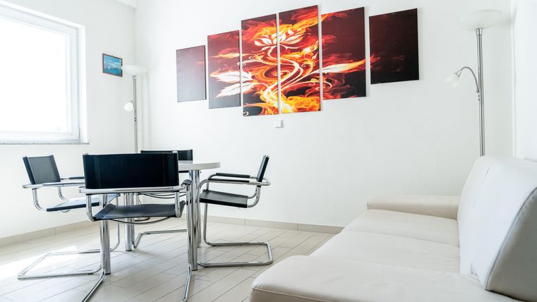Een moderne woonkamer met een witte bank en een glazen tafel. Aan de muur hangen kleurrijke schilderijen die levendige oranje en rode tinten tonen.