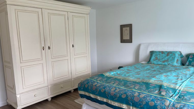 Une chambre confortable avec une grande armoire blanche et un lit avec une couette bleue. Les murs sont clairs et le sol est en bois.