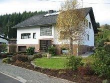 A modern residential building with a colorful garden and an adjacent parking lot. The facade is partially in white and brown.