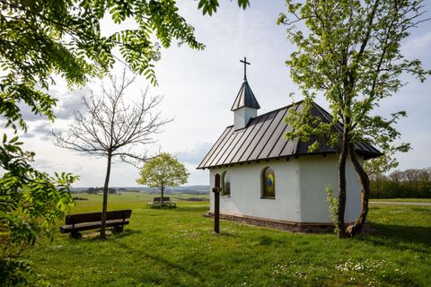 Eine kleine Kirche umgeben von grünen Wiesen und Bäumen. Im Hintergrund ist ein klarer Himmel zu sehen.