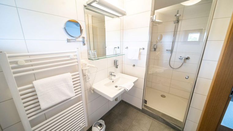 Een modern badkamer met een lichte tegelvloer. Het heeft een douche, een wastafel en een handdoekhouder.