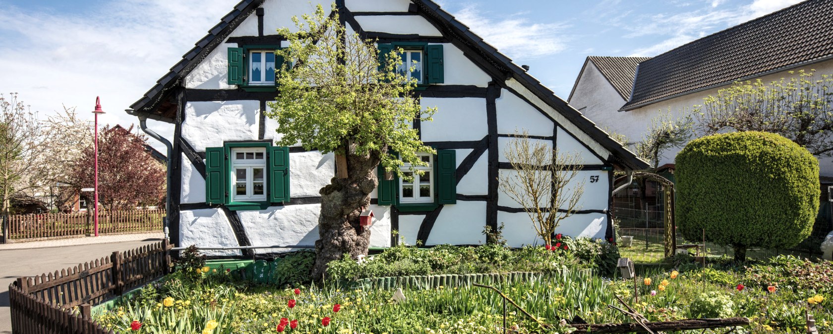 Ein traditionelles Fachwerkhaus in Pomster mit gr&uuml;nem Garten und bunten Blumen, umgeben von einem Holzzaun unter blauem Himmel., &copy; VGVAdenau,W.Klein