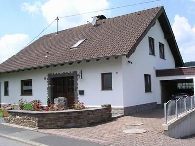 A beautiful house with a modern design and a gabled roof. The front yard is landscaped with flowers and stones.