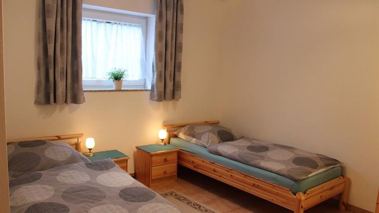 A simple bedroom with two beds and a window. There is a small table and a houseplant on the windowsill.