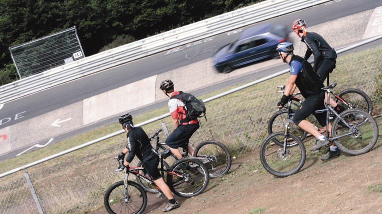 Vier Mountainbiker beobachten ein Auto auf einer Rennstrecke.