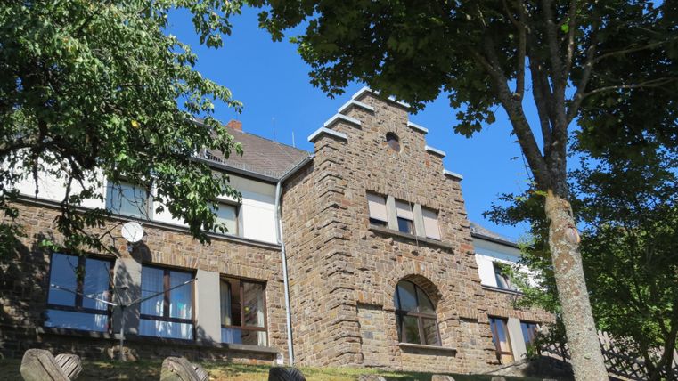 Ein modernes Gebäude aus Stein, umgeben von Bäumen. Der Himmel ist klar und blau.