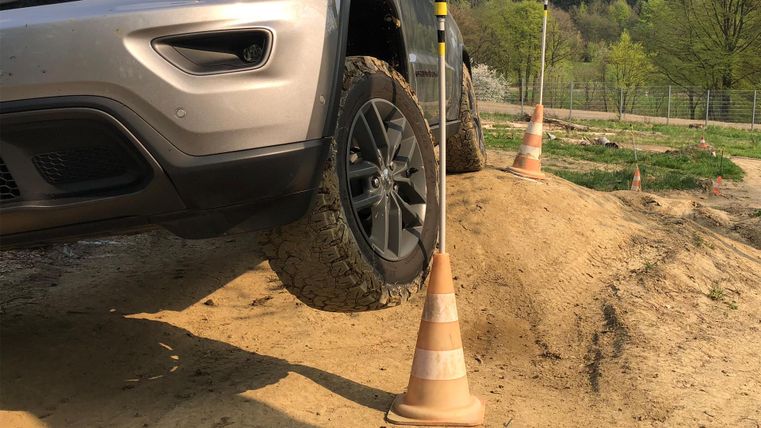 Ein Geländewagen fährt über eine unebene Oberfläche. Ein Teil des Fahrzeugs schwebt über dem Boden, während ein Verkehrshütchen daneben steht.