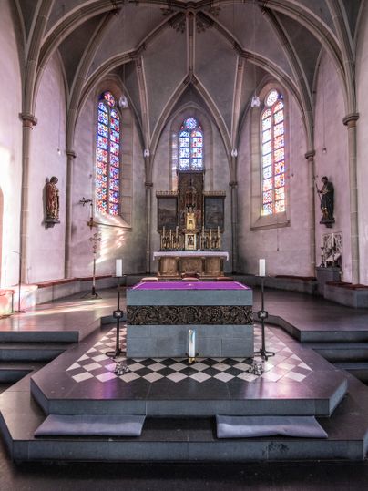 Innenansicht einer Kirche mit Altar und bunten Glasfenstern.