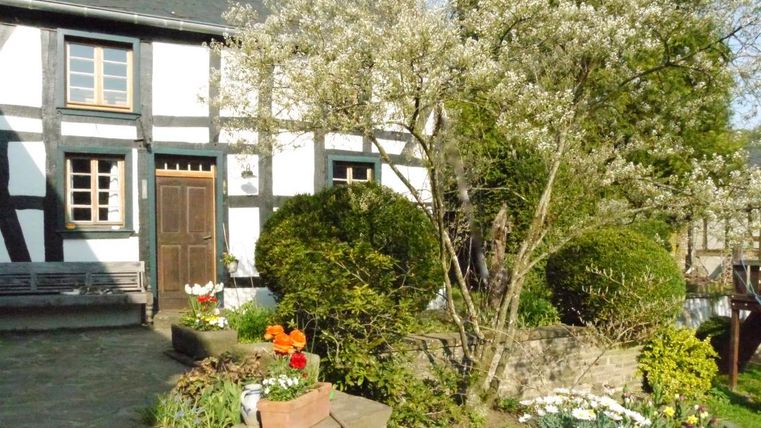 A beautifully designed garden with a half-timbered building. Flowers and bushes frame the entrance area.