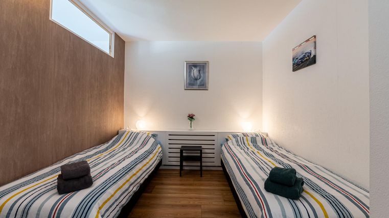 Een eenvoudige kamer met twee eenpersoonsbedden en gestreepte dekbedden. Er is een klein plantje en foto's aan de muren.