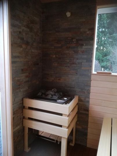 A cozy room with a sauna and a wooden stove. The walls are made of natural stone and wood, with a window for natural light.